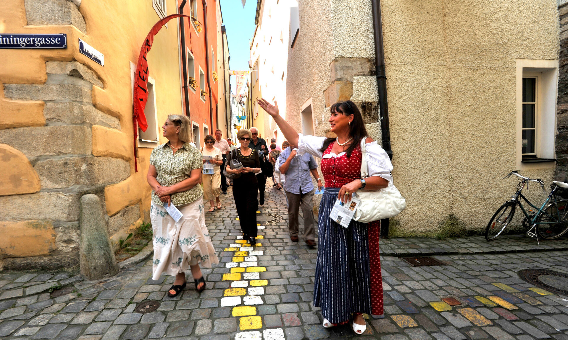 Eine Gruppe von Menschen spaziert durch die bunte Kopfsteinpflasterstra&szlig;e in Passaus Altstadt.